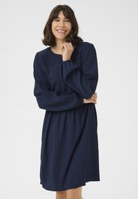 Navyblå klänning i textil med struktur. Har lång ärm, rund halsringning och en avslappnad passform med ett cinchat midja.