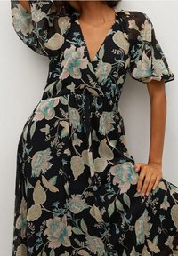 Robe noire à fleurs avec un décolleté en V, des manches courtes bouffantes et un design fluide. Elle arbore des motifs de fleurs pastel et une taille froncée.