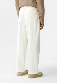 Weiße weite Hosen mit glatter Textur, ausgestattet mit Gesäßtaschen und einem Bund, kombiniert mit beigen Slippern.