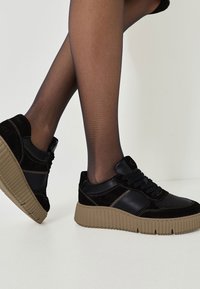 Svarta sneakers i en kombination av slät och mocka läder, upphöjd gummisula, snördesign och dekorativa sömnadsdetaljer.