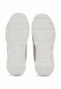 Baskets en tissu gris avec des semelles en caoutchouc blanc. Les semelles présentent un motif de grip texturé et une étiquette de logo sur le côté.