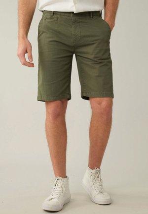 Shorts vert olive en tissu mélangé coton, dotés de deux poches avant et d'une coupe droite, associés à des baskets montantes blanches.