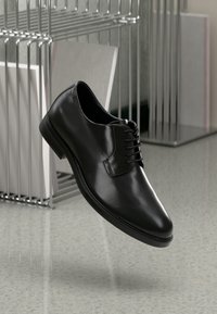 Scarpa da uomo in pelle nera con finitura liscia, punta arrotondata e design classico con stringhe. Presenta una suola testurizzata e dettagli di cucitura discreti.
