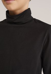 Svart polotröja tillverkad av mjukt tyg. Har en hög krage och sömlös design, med fokus på en slät textur och figurnära passform.