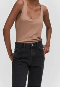 Top sin mangas beige con escote ancho, combinado con unos jeans de mezclilla negros de cintura alta. Los jeans cuentan con bolsillos clásicos y un cierre frontal a botones.