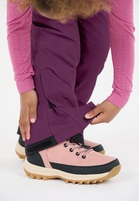 Fuchsia Hosen sind teilweise in hellrosa und schwarze Outdoorschuhe mit einer robusten Sohle gesteckt, die sichtbar anpassbare Klettverschlüsse am Knöchel haben.