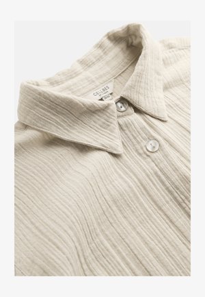Beige textuur overhemd met kraag, voorzien van twee witte knopen en een zichtbaar kledinglabel aan de binnenkant van de halslijn met merk en maat.
