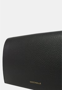 Clutch bag in pelle nera con finitura testurizzata. Presenta una forma arrotondata e un logo del marchio in oro nella parte inferiore.