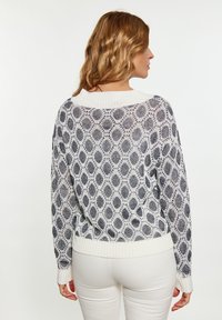 Pulover alb și bleumarin cu un model, cu o croială lejeră, manșete și tiv cu dantelă; prezintă o textură tricotată, asemănătoare cu dantela.