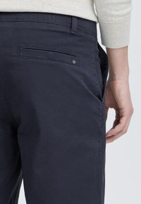 Chinos bleu marine foncé en tissu mélangé de coton. Comprend une poche arrière avec un branding discret et un design à jambe droite.