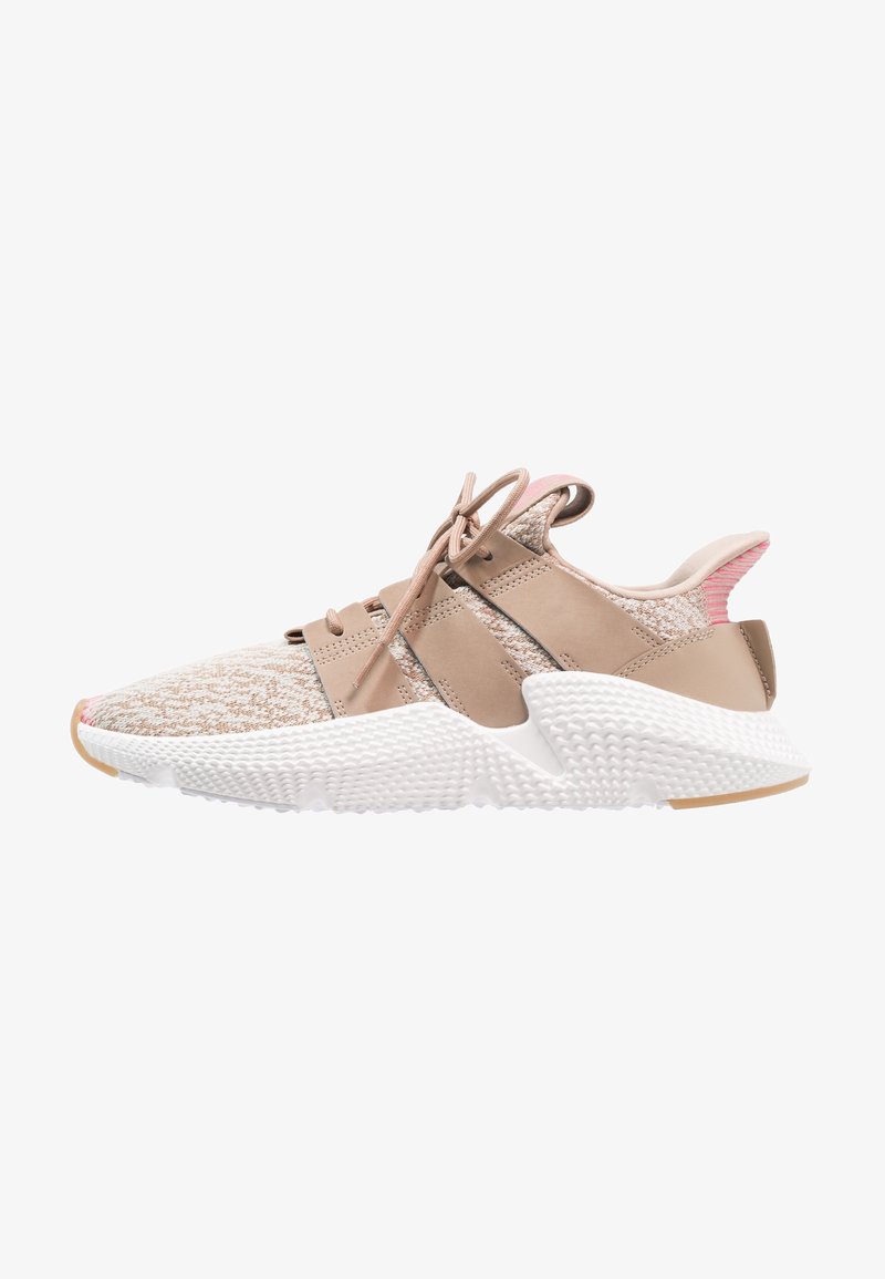Chaussure de sport beige avec un dessus en tricot texturé, des accents en cuir beige et une semelle en caoutchouc texturée blanche. Présente des détails roses au niveau du talon.