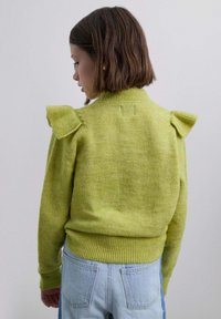 Suéter verde de punto con detalles de volantes en los hombros, tejido texturizado, cuello alto y dobladillo acanalado, combinado con jeans de mezclilla azul claro.