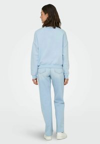 Lichtblauwe sweatshirt met een geribbelde zoom, relaxed fit en verlaagde schouders, gecombineerd met lichtblauwe rechte jeans en witte sneakers.