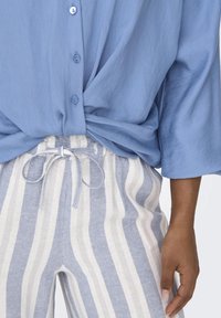 Ljusblå skjorta med knappar i lös passform och uppvikta ärmar, kombinerad med randiga ljusblå och vita byxor med dragsko.