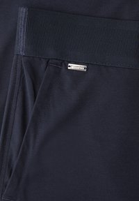 Detail kapsy námořnicky modrých kalhot s elastickým pasem a malou stříbrnou značkou "Street One" nad kapsou.