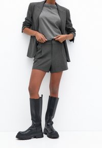 Veste grise et short assorti en tissu texturé, combinés avec des bottes noires montantes jusqu'au genou, dotées d'une semelle épaisse et de panneaux latéraux élastiques.