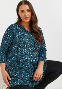 Tunic a maniche lunghe nera con motivo astratto in teal e bianco. Presenta un colletto con bottoni, tessuto morbido e vestibilità rilassata.