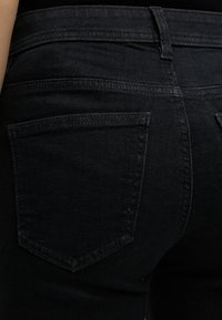 Κοντινό πλάνο ενός ατόμου που φοράει μαύρο τζιν παντελόνι, δείχνοντας τις λεπτομέρειες της πίσω τσέπης και της μέσης.