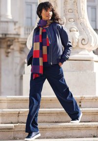 Marine bomberjack, rood-en-blauw geblokte sjaal, marine corduroy broek met brede pijpen en donkere sneakers, tegen een achtergrond van stenen trappen.