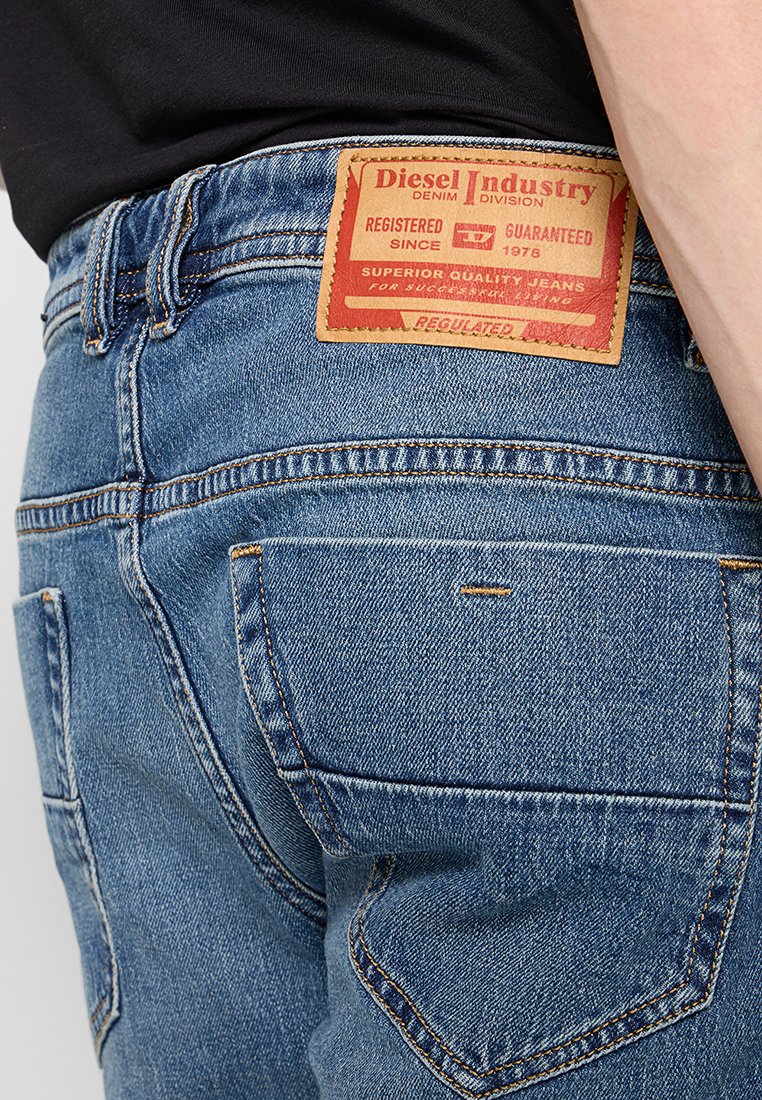 Gros plan sur la poche arrière d'un jean en denim bleu avec une étiquette de marque Diesel Industry marron sur la taille.