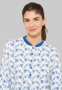 Camicia bianca con motivo floreale blu, colletto blu arrotondato e bottoni sulla parte frontale. Tessuto morbido con una vestibilità comoda.