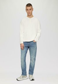 Chemise henley blanche à manches longues avec trois boutons, jean en denim bleu et baskets grises avec des détails en mesh. Tenue simple et décontractée.