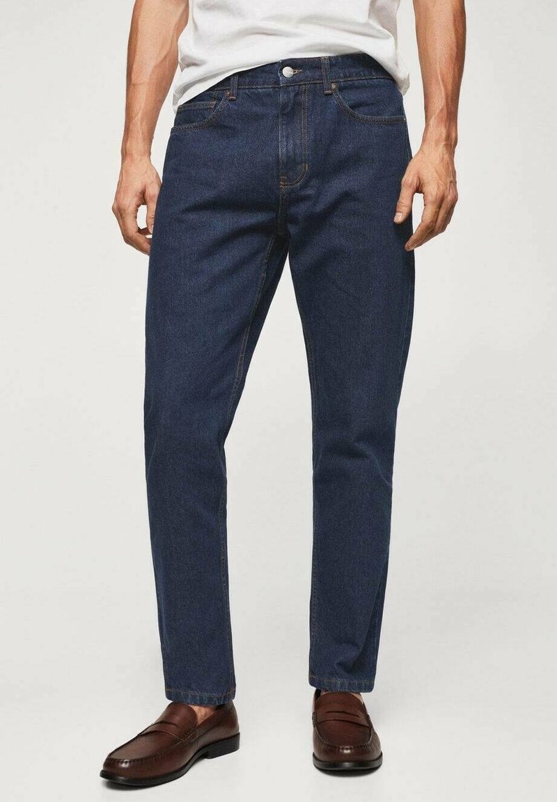 Vaqueros de mezclilla azul oscuro con corte recto, diseño estándar de cinco bolsillos y costuras en contraste, combinados con mocasines marrones.