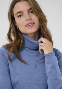 Light blue knit turtleneck sweater with ribbed accents at the neck and cuffs, featuring a smooth texture and a fitted design.