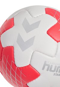 Vit och röd fotboll med pentagonal form, utrustad med texturerade paneler, rutmönster och präglade grafiska detaljer som inkluderar pilar och varumärkeslogotyper.