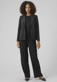 Schwarzer Cordblazer mit Revers und zwei vorderen Taschen, kombiniert mit schwarzen weiten Hosen und schwarzen spitzen Ballerinas.