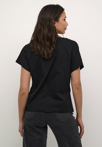 T-shirt noir en coton à manches courtes, coupe décontractée et col rond. La vue de dos montre des coutures minimales et une texture lisse.