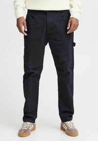 Navy blue cargo pants made of cotton blend, featuring side pockets and a relaxed fit, paired with gray sneakers and a cream sweater.