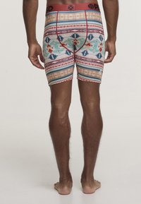 Boxer da uomo multicolori con motivi geometrici e tribali, elastico rosso in vita, materiale elasticizzato, design fitted, lunghezza a metà coscia.