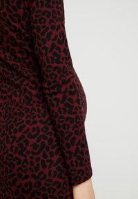 Maglione bordeaux con motivo a leopardo nero, maniche lunghe e texture morbida. Il tessuto si adatta strettamente alla forma del corpo.