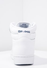 Baskets montantes blanches en cuir avec un col rembourré, logo Reebok au talon et semelle en caoutchouc texturée. Design simple avec une finition lisse.