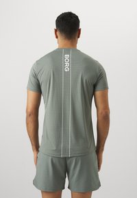 Sivo športno majico s kratkimi rokavi, ki vsebuje vertikalni beli logotip "BORG" in teksturiran vzorec na hrbtni strani. V kompletu s usklajenimi kratkimi hlačami.