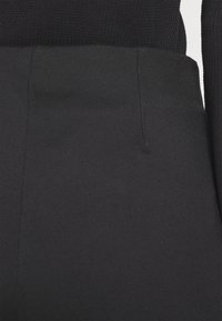 Schwarze hochtaillierte Hosen mit glatter Textur, die über einen Bund, seitliche Nahttaschen und minimale Nähdetails verfügen.