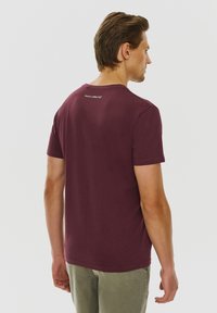 Bordowa koszulka z krótkim rękawem wykonana z bawełny, z okrągłym dekoltem. Posiada delikatne logo marki z tyłu, blisko dekoltu.