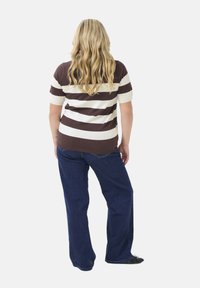 Gestreiftes kurzärmliges Oberteil in Braun und Creme mit lockerer Passform; kombiniert mit dunkelblauen weiten Jeans; Modell von hinten gesehen.