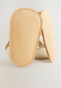 Leather shoes with a tan suede sole, featuring a simple design and rounded edges. The upper part is smooth with a neutral color palette.