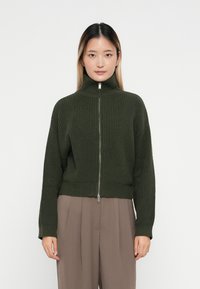 Maglione a coste di un verde scuro, con colletto alto e zip completa. Design cropped con maniche lunghe e tessuto testurizzato.