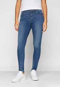 Blå skinny jeans i denim med en slät textur, med en klassisk femfickdesign och subtila sömmar. Matchas med vita sneakers.