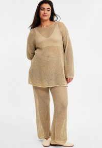 Beige netgebreide top met een brede halslijn, gecombineerd met bijpassende wijde broek. De stof heeft een open weefpatroon voor ademend vermogen.