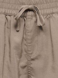 Nærbillede af beige bukser med elastisk taljebånd, snørebånd bundet og synlige syningsdetaljer.