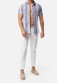 Short-sleeve, multicolored striped shirt in cotton. Features blue, white, and reddish stripes. Paired with white linen pants and gray espadrilles.