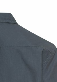 Donkerblauwe shirt met een kraag. Heeft een gestructureerde stof met een subtiele glans. Zichtbare stiksels langs de schouder en naaddetails.
