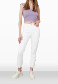Top corto morado acanalado con tirantes anudados en los hombros, combinado con jeans blancos de cintura alta y zapatillas blancas con suela texturizada.