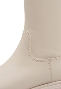 Bottine en cuir beige avec une texture lisse, présentant une silhouette arrondie et des coutures visibles sur le côté et le talon pour plus de durabilité.