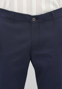 Pantaloni blu navy con una texture liscia, dotati di chiusura a un bottone, passanti per cintura e tasche frontali.