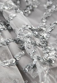 Tissu en tulle gris embellit de sequins argentés, présentant un motif complexe de cercles dispersés et une texture lisse.